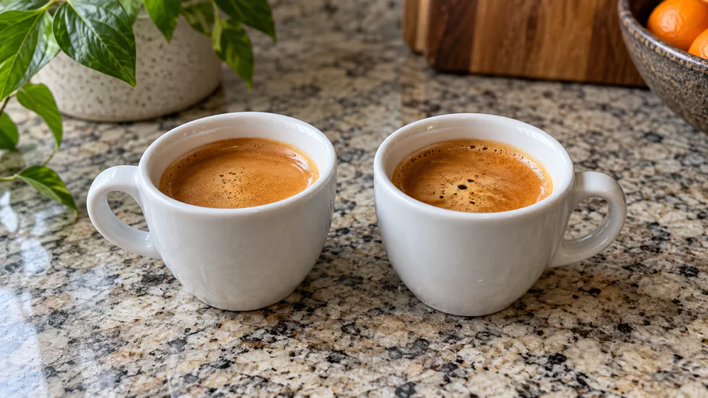 Two double espressos in identical ceramic cups side by side, both topped with golden crema, one pulled on each machine.