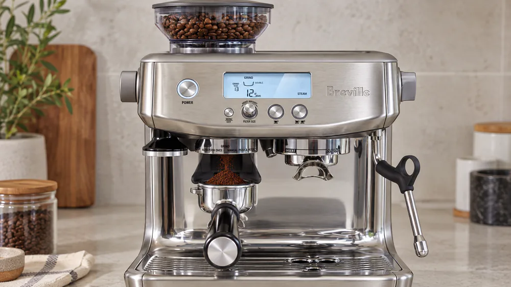 Close-up of the Breville Barista Pro's bean hopper and conical burr grinder chute with freshly ground espresso dosing into the 54 mm portafilter.