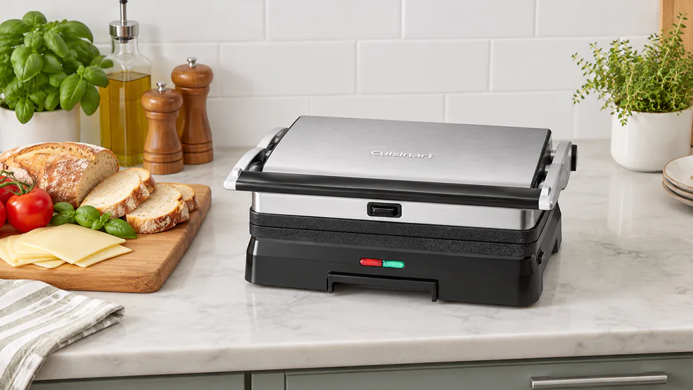 Closed Cuisinart Griddler GR-11NAS on a kitchen counter next to a cutting board with sandwich bread and cheese