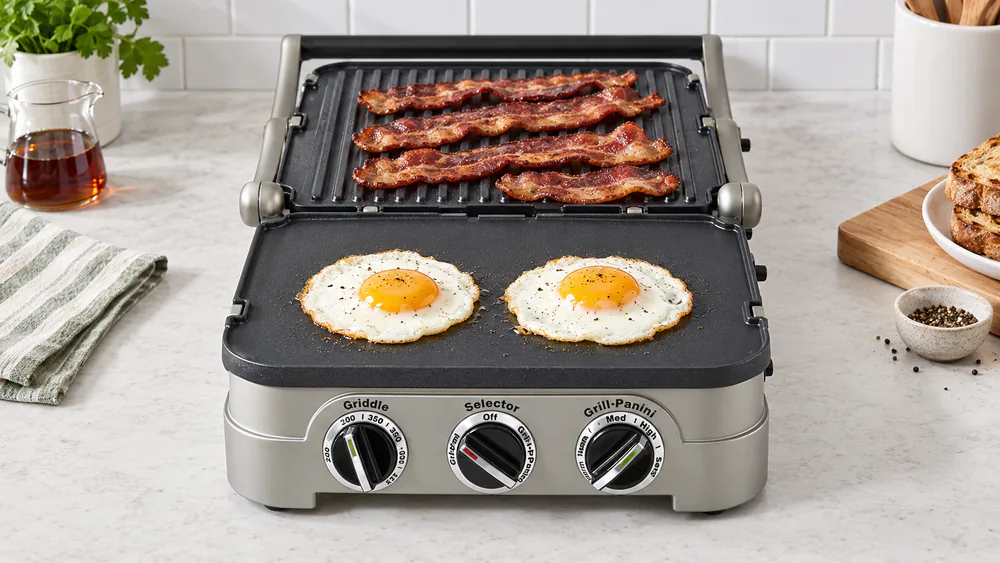 Cuisinart Griddler opened flat with bacon on the ribbed plate and fried eggs on the flat plate, red power light and green ready light visible