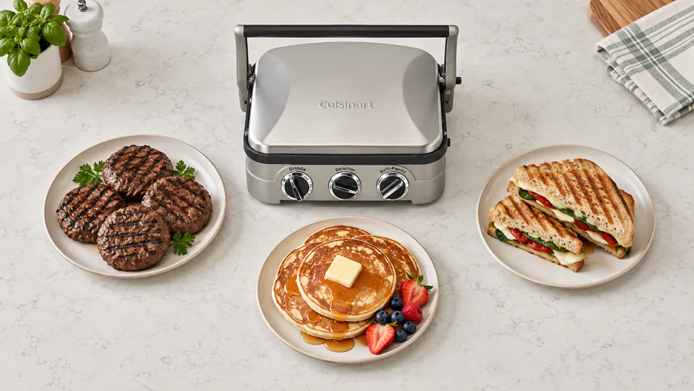 Overhead view of the Cuisinart Griddler 5-in-1 on a kitchen counter beside plated burgers, pancakes and a pressed sandwich used for testing