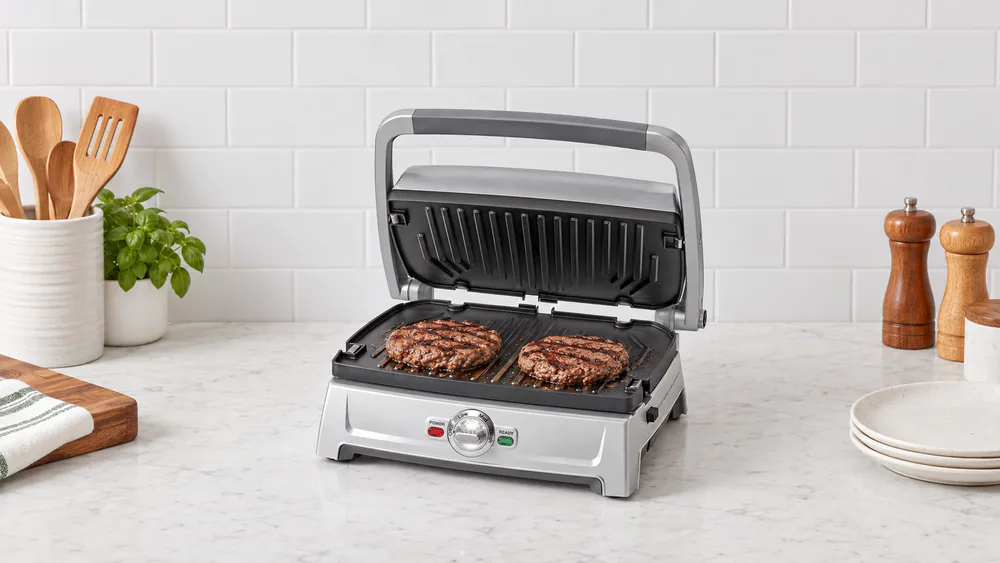 Two burger patties browning on the open nonstick plates of the Cuisinart Griddler Compact