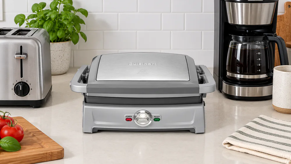 The Cuisinart Griddler Compact closed on a crowded kitchen counter beside a toaster and coffee maker