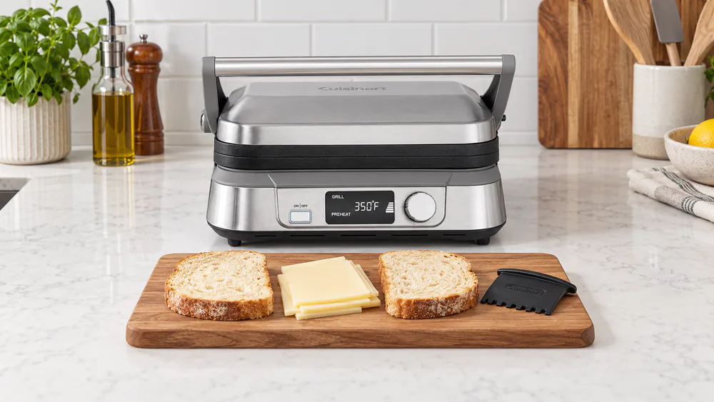 Cuisinart Griddler Five on a kitchen counter with sliced bread, cheese and a scraper laid out before a panini test