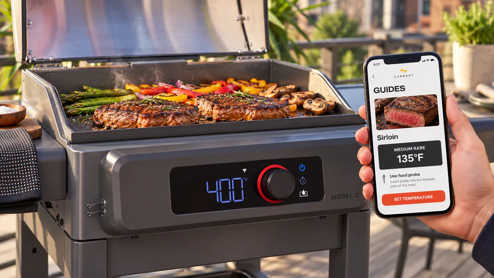 Close-up of the Current Model G Electric Griddle temperature dial and display with a phone showing the CURRENT app beside it
