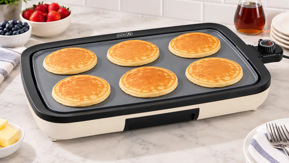 A batch of golden pancakes cooking in rows on the Dash ceramic griddle, edges and center browned the same