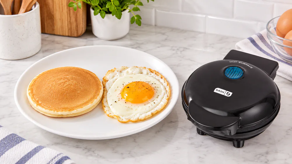 A single small round pancake and a fried egg side by side on a plate, both cooked on a 4-inch Dash Mini Maker griddle