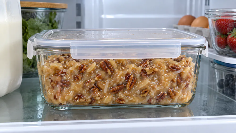 A glass airtight container filled with coconut pecan frosting, ready to be stored in the refrigerator.