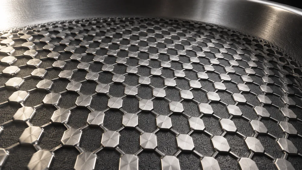 Macro close-up of a hexagon-patterned hybrid pan surface, raised stainless steel peaks surrounding a nonstick valley.