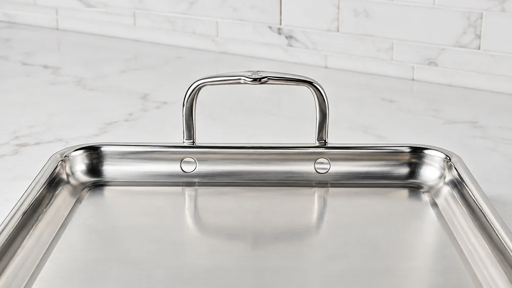 Close-up of the Hestan Provisions griddle showing the drip channel along the flared rim and the flush rivets on the wide handle