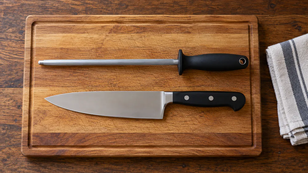 A steel honing rod and chef’s knife resting separately on a dry cutting board
