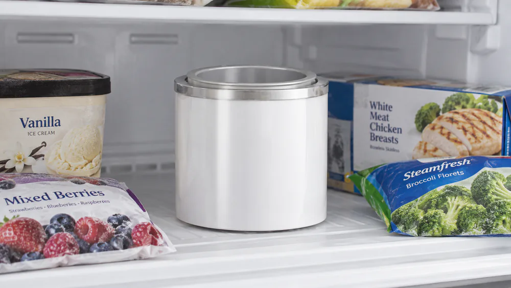 A Cuisinart double-insulated ice cream freezer bowl sitting on a cleared freezer shelf surrounded by frozen food, chilling overnight before churning.