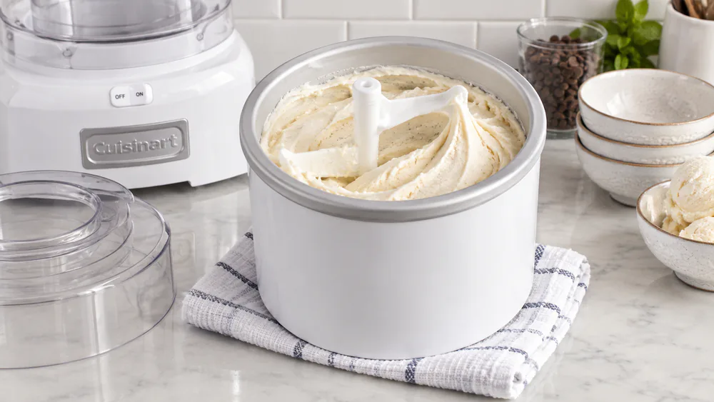 Freshly churned vanilla ice cream at soft-serve consistency inside a Cuisinart freezer bowl, the paddle leaving a swirled trail through the thick mixture.