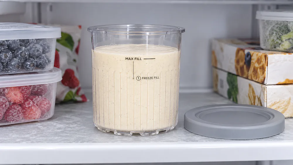 A Ninja Creami Deluxe 24 oz tub sitting level and upright on a flat freezer shelf, base frozen solid and flat on top.