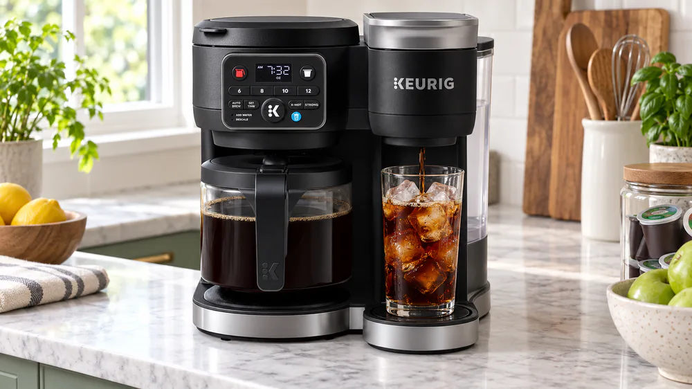 A tall glass full of ice under the Keurig K-Duo Gen 2 spout mid-brew, the iced coffee pouring over the ice, front control panel glowing.