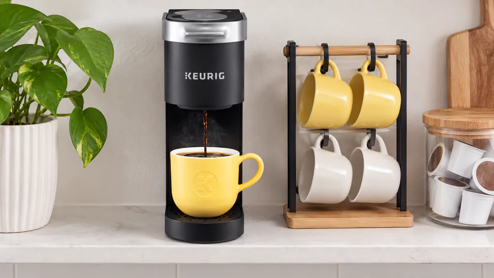 A Keurig K-Mini on a narrow shelf, taking less room than the mug rack beside it.
