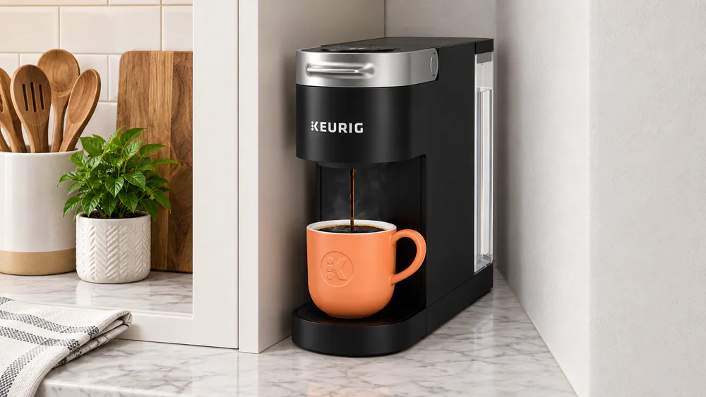 The Keurig K-Slim in black sitting in a narrow gap between a cabinet and a wall.