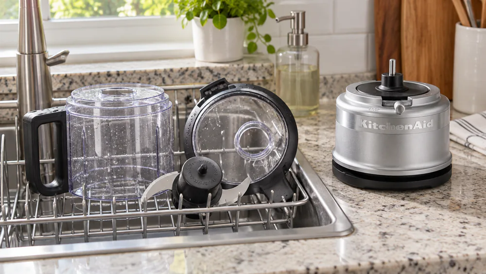A clean KitchenAid food chopper work bowl and blade drying on a dish rack, plastic clear and unclouded after repeated washes.