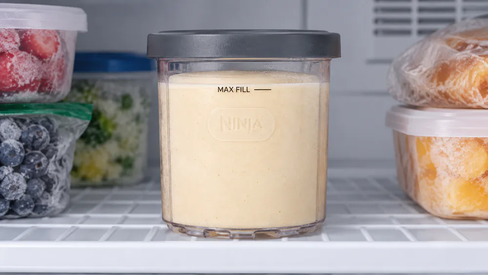 A Ninja Creami pint frozen flat in the freezer for 24 hours, base frozen solid to the MAX FILL line.