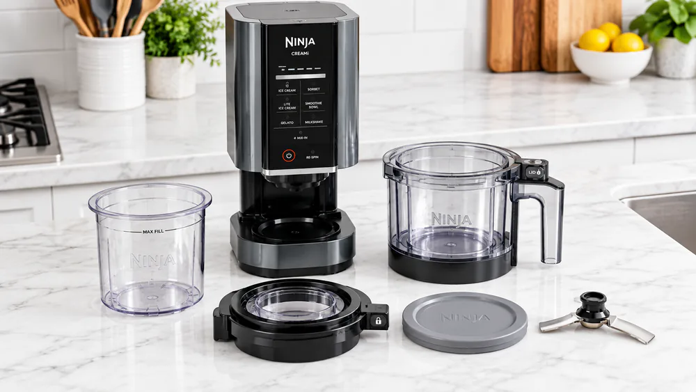 The Ninja CREAMi motor base, empty 16-ounce pint, outer bowl, and Creamerizer Paddle laid out on a kitchen counter before first use.