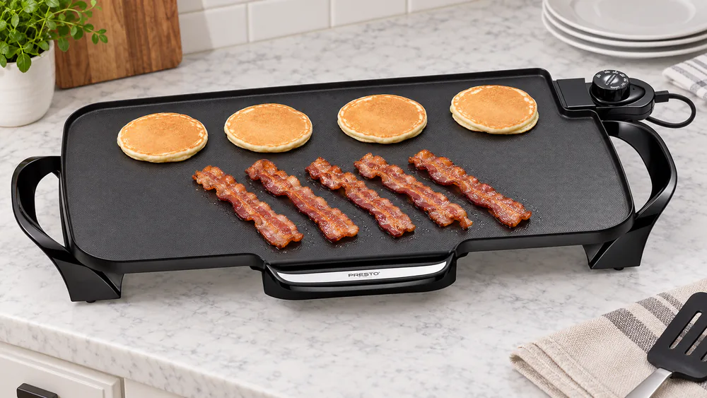 Bacon strips on the drip-tray side and pancakes on the far side of the Presto 22-inch griddle at the same time