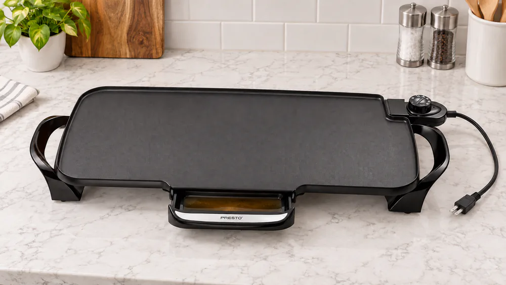 The slide-out plastic drip tray of the Presto 22-inch griddle pulled halfway out, with bacon grease collected inside