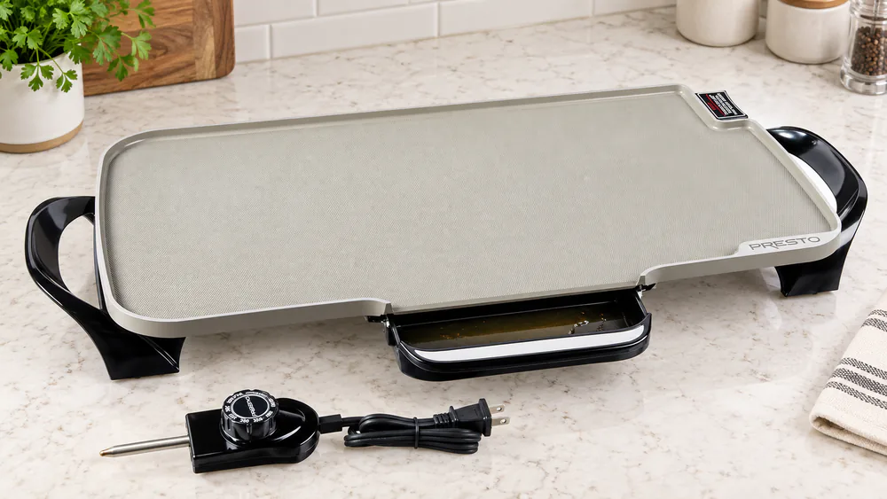 The plastic slide-out drip tray of a Presto 07062 griddle pulled halfway out, holding bacon grease