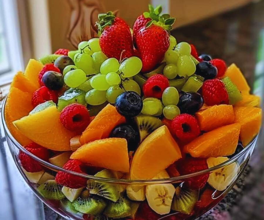 A colorful glass bowl filled with a variety of fresh fruits, including strawberries, grapes, blueberries, and kiwi slices.