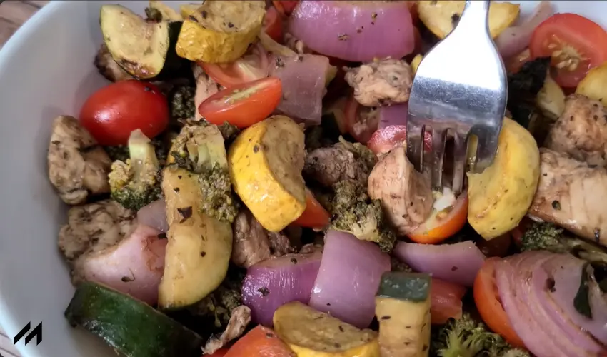 A close-up of a colorful dish featuring roasted chicken, broccoli, zucchini, yellow squash, red onion, and cherry tomatoes.