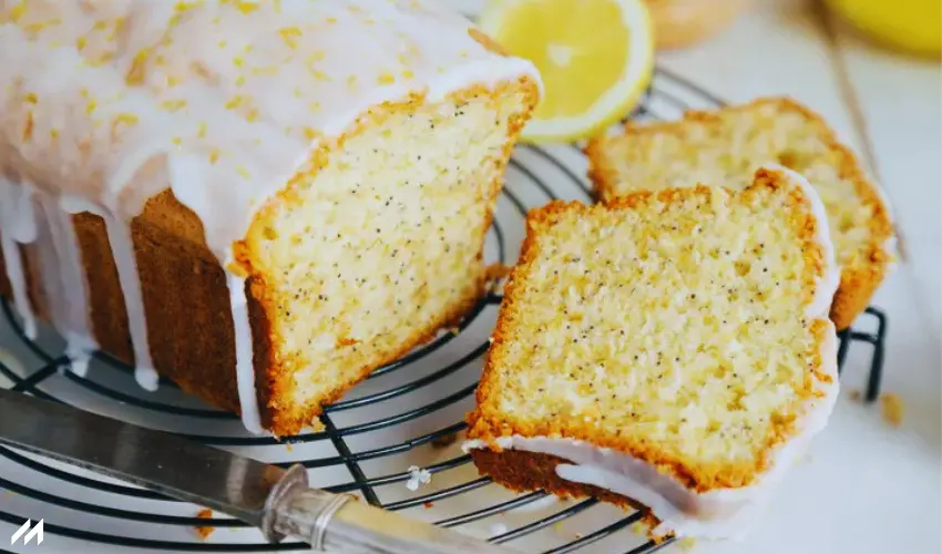 Chia Seed Lemon Zest Bread A lemon poppy seed loaf cake, glazed with icing, sliced and resting on a cooling rack beside fresh lemon slices.