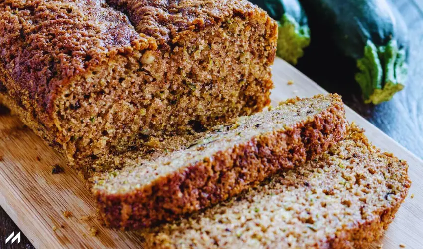 Coconut Flour Zucchini Bread Freshly baked zucchini bread, sliced and arranged on a wooden board, with whole zucchinis in the background.