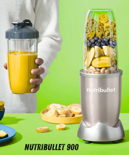 A person holds a smoothie cup beside a NutriBullet 900 blender filled with fruits and nuts against a bright green background.