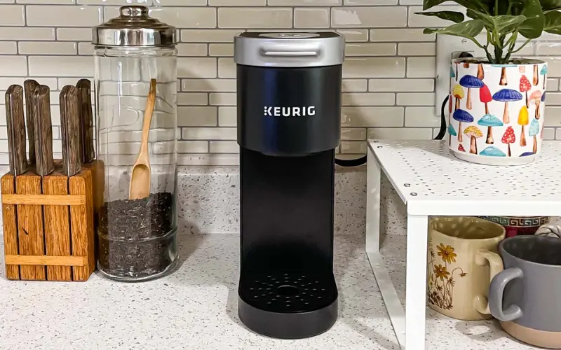 Keurig K-Mini single-serve coffee maker on a kitchen countertop with mugs and coffee accessories.