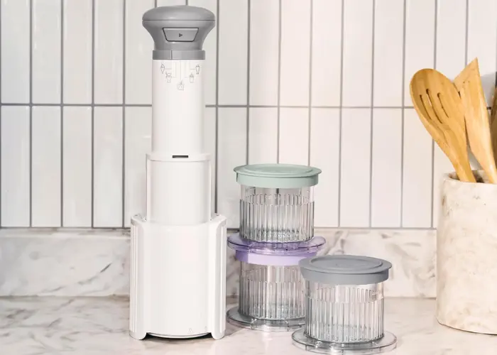 Cuisinart FastFreeze 5-in-1 Ice Cream Maker Review Cuisinart FastFreeze 5-in-1 Ice Cream Maker on white countertop with gray handheld FreezeWand on detachable base, surrounded by three stacked half-pint glass dessert cups with colorful lids (green, purple, gray) and wooden utensils nearby.