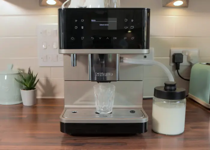 Miele CM 6360 automatic coffee machine on a kitchen counter with a glass under the spout and a milk container attached.
