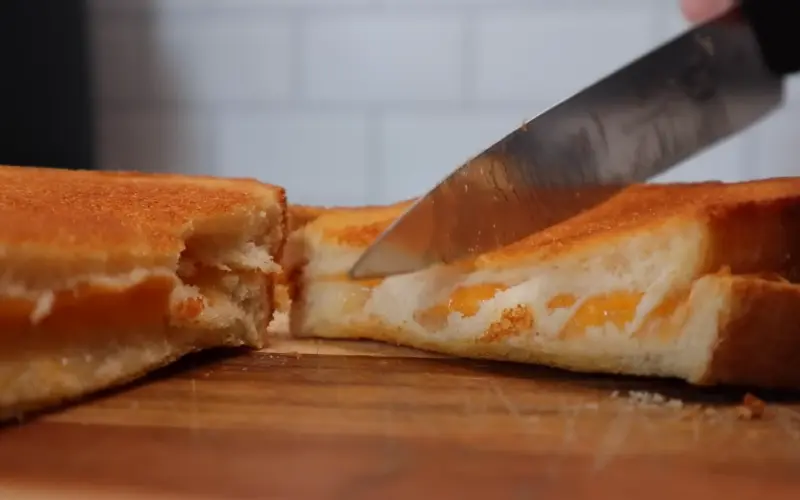 Air Fryer Grilled Cheese Sandwich Recipe Golden crispy air fryer grilled cheese sandwich cut in half showing melted cheese stretching between slices on wooden cutting board