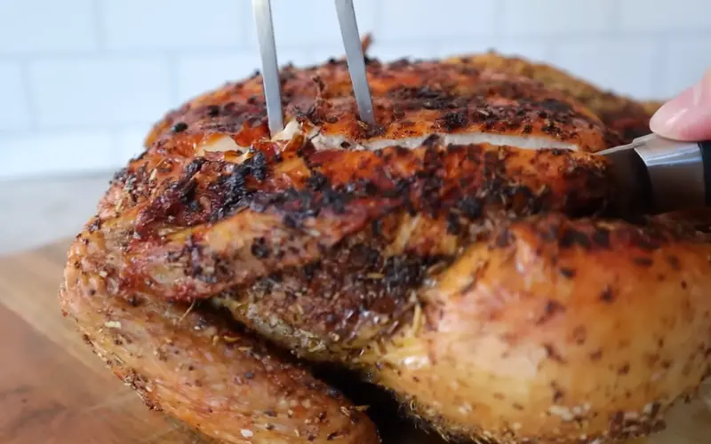 Juicy air fryer whole chicken with golden crispy skin being sliced with kitchen tongs on wooden cutting board